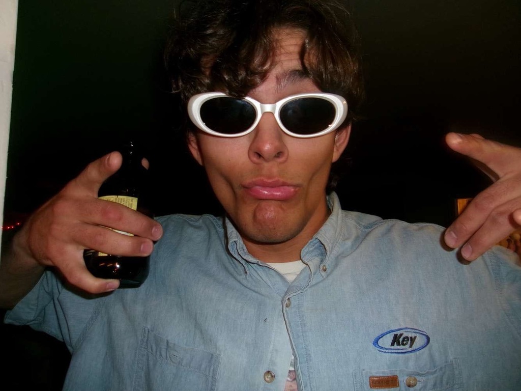Guy in white sunglasses and a denim work shirt, beer in hand, making a duck face at the camera